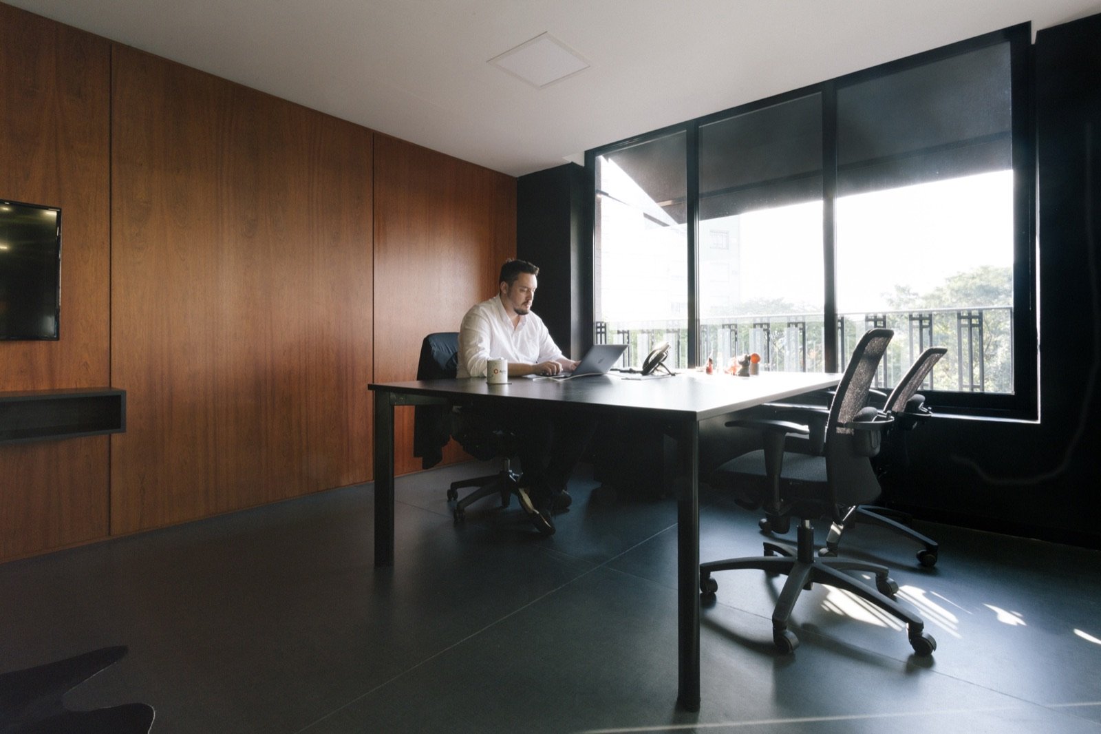 A wood-panelled meeting room with a person working on a laptop by the window