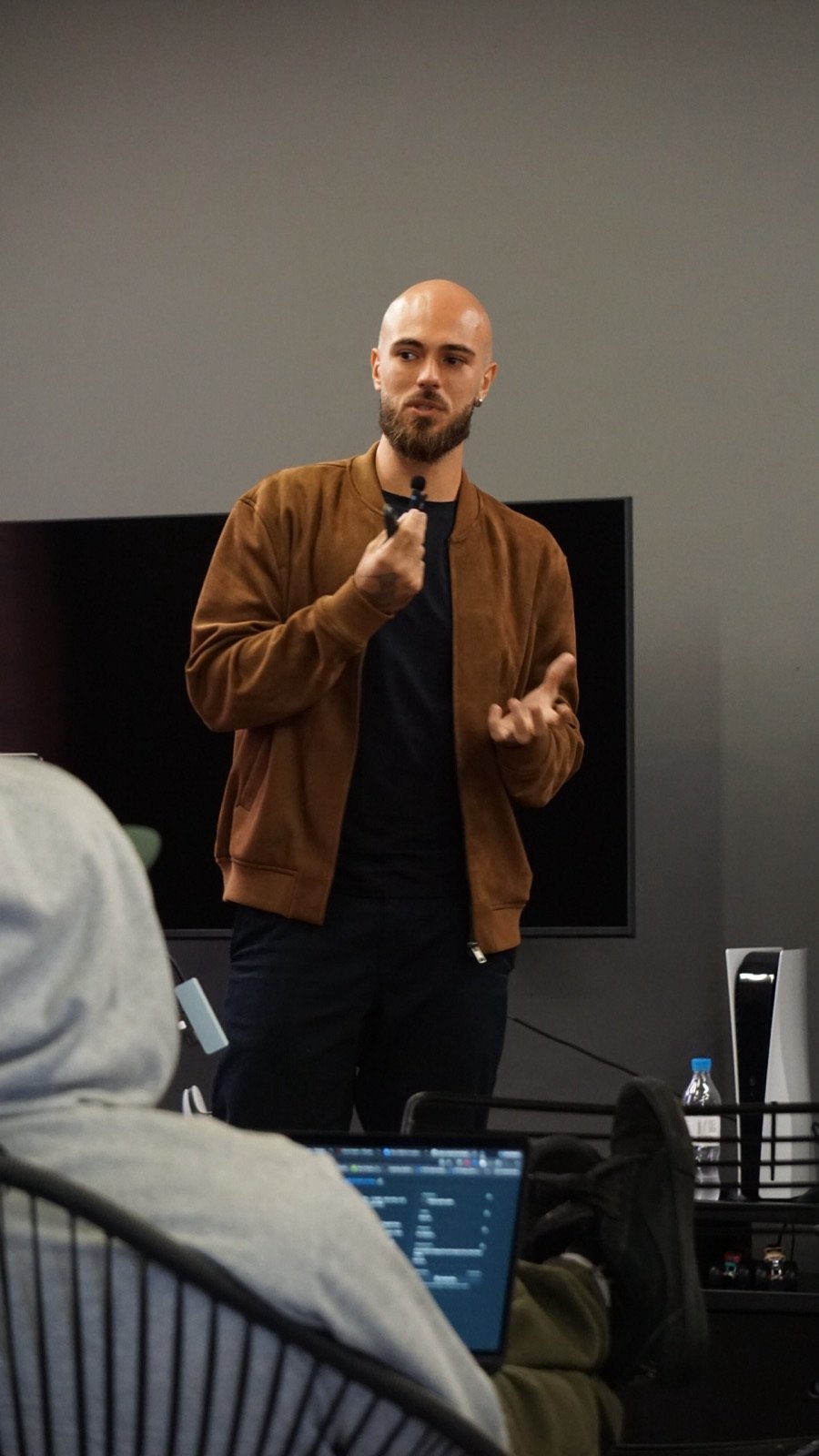 A team member giving a talk in front of a screen while colleagues listen with laptops